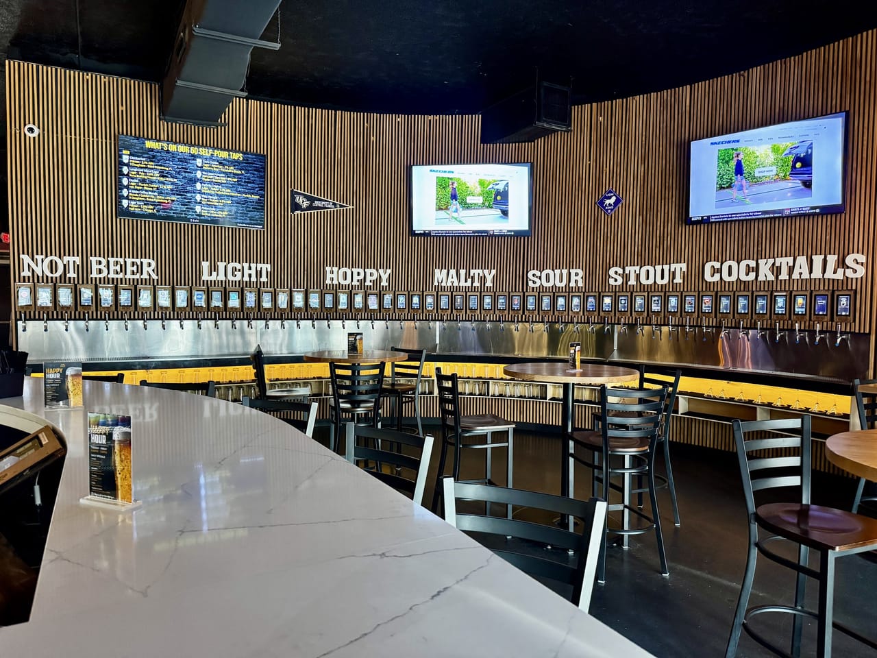 Wide view of the self-pour tap wall from the white marble bar at Pour Choice Taphouse in Mills 50 Orlando