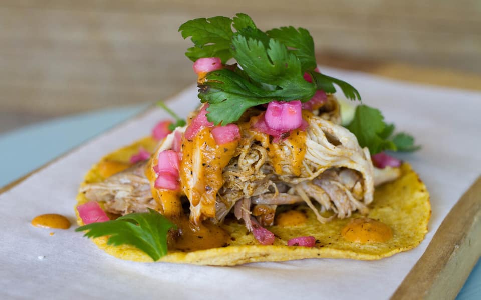 Black Rooster Taqueria taco with shredded meat, orange crema, pickled onions, and cilantro