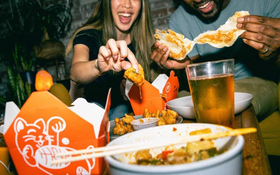 Hawkers Asian Street Food takeout boxes, roti, and dumplings shared at a table